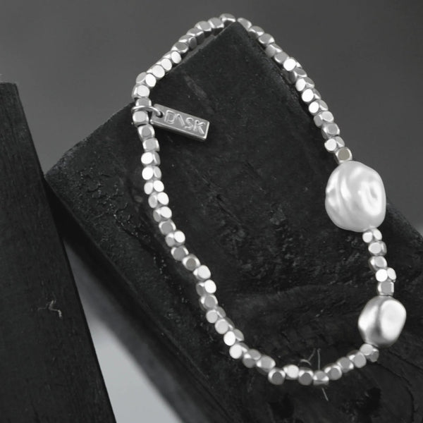 Silver beaded bracelet with a pearl on a black textured surface